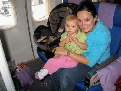Toddler sitting in a car seat installed on an airplane seat during a long-haul flight"