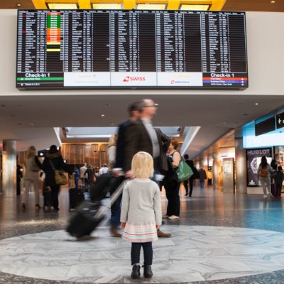 Young child standing in the departures hall at Zurich Airport looking up at the flight information board